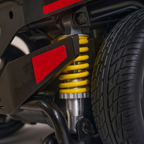 Close-up of Buzzaround XL+ 4-Wheel Mobility Scooter suspension system with yellow shock absorber and red accents.