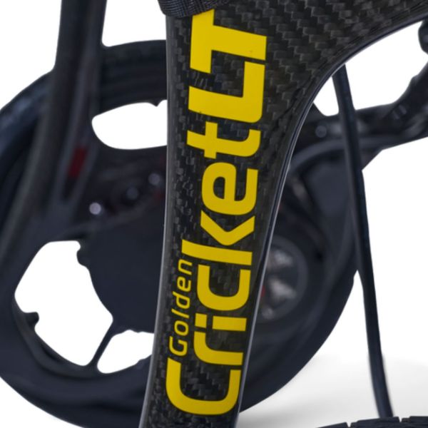 Close-up of a carbon fiber frame with bold yellow 'Golden Cricket LT' branding, showing the textured weave pattern and part of the wheel in the background.