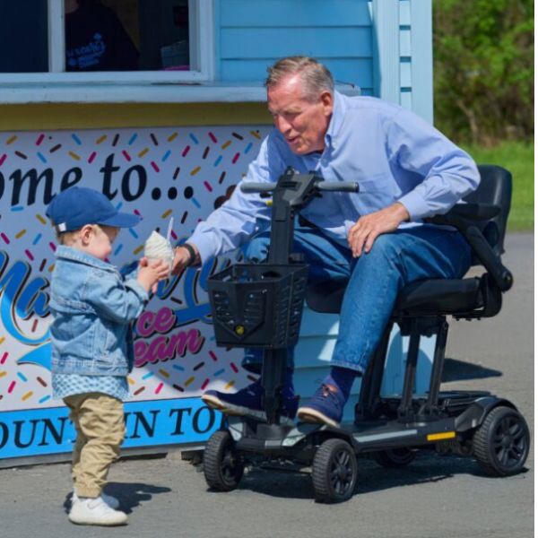 Golden Technologies Buzzaround Carry On HD Folding Mobility Scooter with a Man Seating on it