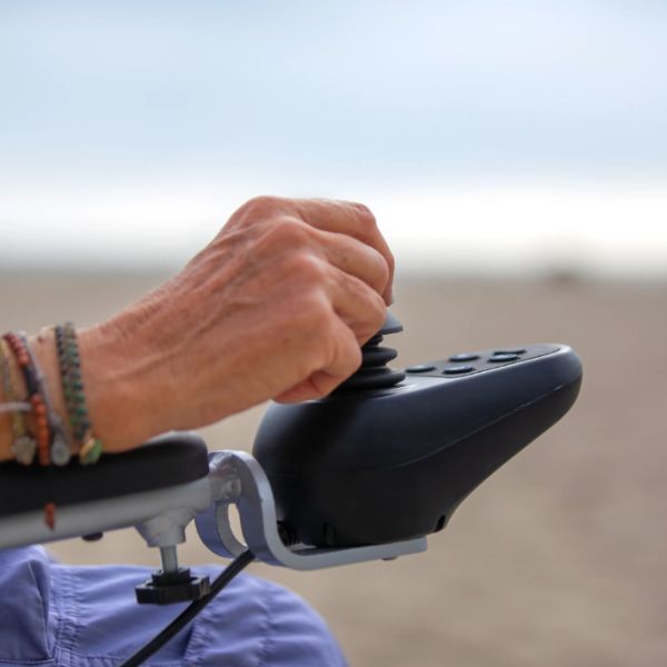 A Hand Holding the Joystick Controller of the Reyhee Superlite Wheelchair with Beach Background