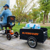 Person using a Superhandy Explorer Heavy-Duty Mobility Scooter with a attached black trailer in an outdoor setting.