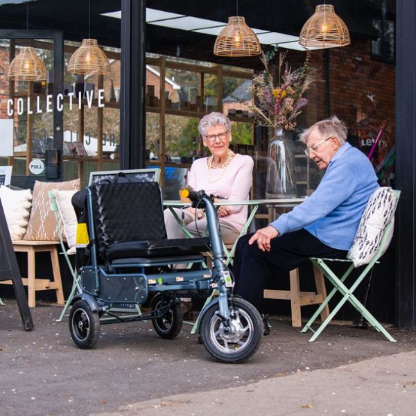 Man and lady sitting with the eFOLDi Explorer Ultra Lightweight Mobility Scooter next to them